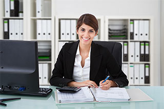 Smiling businesswoman at a desk with accounting documents and a computer in an organized office.