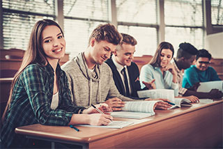 Smiling students sitting in a lecture hall, studying and taking notes together.