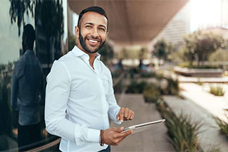 Smiling young man in a white shirt using a tablet in a modern urban setting.