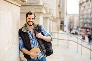 Happy man holding notebooks, standing outdoors with a backpack.