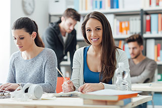 Smiling female student in a classroom with peers working in the background.